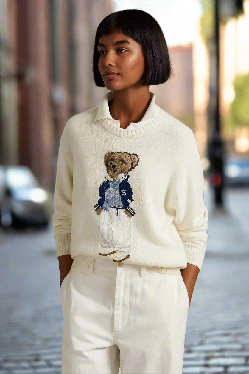 Woman wearing a cream sweater with a teddy bear design on a city street.